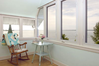 A picture of a rocking chair with a quilt draped over it in a room with a lake seen through the windows 